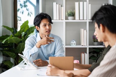 Modern ofis ortamında mali stratejiler ve tasarruf planları hakkında tartışan iki genç profesyonel.