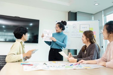 UX UI projesinde işbirliği yapan çeşitli tasarımcılardan oluşan bir ekip, modern ofis ortamında kablolar ve prototipleri tartışıyor..