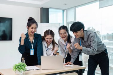 Bir grup genç profesyonel modern ofiste başarılı bir başarıyı kutlarken bir dizüstü bilgisayarın etrafında toplandılar..