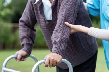 Yaşlı bir hasta, bir bakıcıdan destek alırken, dışarıda yürüyen birini kullanarak, sağlık hizmetlerini ve yardımlarını ön plana çıkarıyor..
