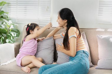 Bir anne ve küçük kızı, yumuşak yastıklarla çevrili, aydınlık bir oturma odasındaki rahat bir kanepede keyifli bir anı paylaşıyorlar..