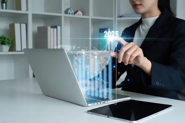 stock image Businesswoman using laptop to analyze financial data with futuristic graphs and 2025 projection in a modern office setting.