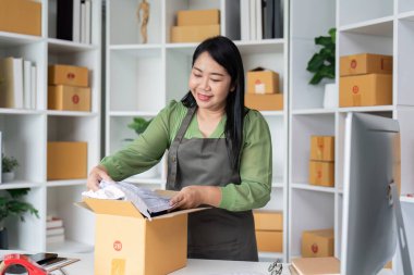 Küçük bir işletme sahibi, karton kutular ve bir bilgisayarla çevrili ev ofisinde sipariş topluyor ve girişimci ruhunu sergiliyor..