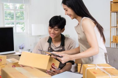 Parlak, modern bir ofis ortamında çevrimiçi siparişler için kutu paketlemek için birlikte çalışan genç bir adam ve kadın..