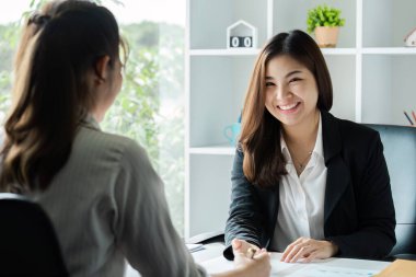 Modern ofis ortamında iki iş kadını, bir toplantıda, gülümsüyor ve belgeleri ve fikirleri tartışıyor..