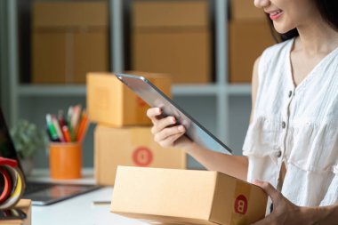 Genç bir girişimci, çevrimiçi işlerini yönetmek için bir tablet kullanır. Çevresi, modern bir ofis ortamında kargo kutularıyla çevrilidir..