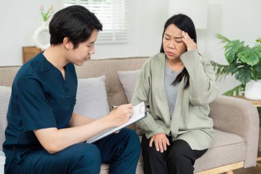 Bir sağlık uzmanı, konforlu bir oturma odası ortamında bir hastaya tıbbi danışmanlık ve destek sağlamak için ev ziyareti yapar..