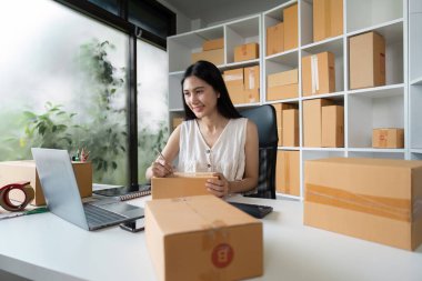 Genç bir iş kadını, küçük işletme ve çevrimiçi satış kavramını gözler önüne sererek, modern bir ev ofisinde nakliyat için paketler hazırlıyor..