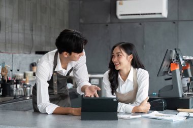 Modern bir kafede iki genç işletme sahibi stratejileri tartışıyor ve bir tablet kullanarak iş kurma planlarını yapıyorlar..