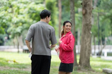 Genç bir çift yemyeşil bir parkta koşuyor, mola veriyor ve birbirlerine gülümsüyor, sağlıklı ve aktif bir yaşam tarzını somutlaştırıyorlar..