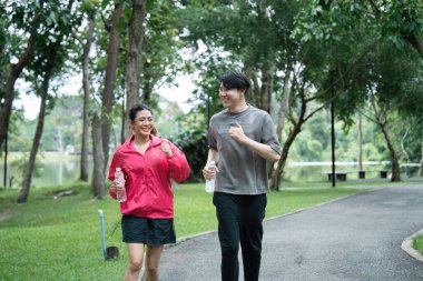 Genç bir çift yemyeşil bir parkta koşuyor, ellerinde su şişeleri, ve birlikte sabah egzersizlerinin tadını çıkarıyorlar..
