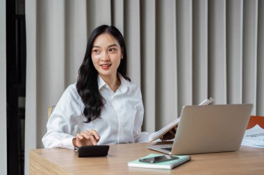 Günümüz ofis ortamında dizüstü bilgisayar ve belgelerle birden fazla iş yapan kendine güvenen iş kadını.