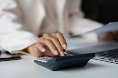 Çağdaş bir ofis ortamında finansal görevlere odaklanarak, hesap makinesi ve laptop kullanan bir kişinin yakın plan görüntüsü.