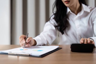 Odaklanmış iş kadını finansal belgeleri inceliyor ve çağdaş ofis ortamında bir masada hesap makinesi kullanıyor..