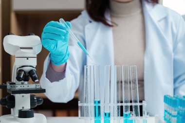 Laboratuvar önlüklü bir bilim adamı deney tüpleri ve mikroskop kullanarak modern bir laboratuvar ortamını gösteriyor..