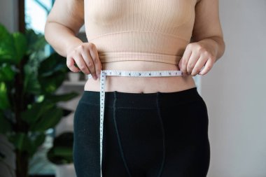 Bir kişinin belini bir mezurayla ölçerken, sağlık ve spor hedeflerine odaklanırken,.