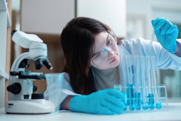 A scientist in a lab coat and safety goggles conducts an experiment using test tubes in a modern laboratory setting.
