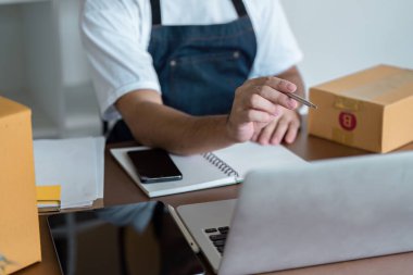 Ev ofis ortamında küçük bir işletme sahibi, dizüstü bilgisayar kullanıyor ve paketleri yönetiyor, girişimciliği ve e-ticareti temsil ediyor..