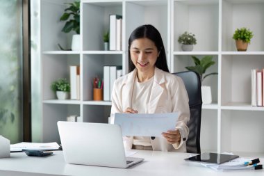 Çağdaş bir ofis ortamında, masasında dokümanları inceleyen kendine güvenen iş kadını profesyonelliği ve odaklanmayı gösteriyor..