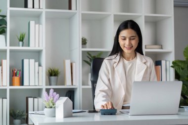 İş kadını dizüstü bilgisayarla finansal verileri hesaplıyor, modern ofis çalışmaları ve profesyonel analizler sergiliyor.