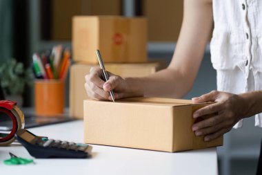 Küçük bir işletme sahibi, ofis malzemeleri ve kutularla çevrili, girişimcilik ve ticareti sembolize eden kargolar hazırlar..