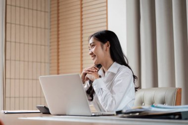 Modern ofis ortamında kendine güvenen bir iş kadını, bir dizüstü bilgisayar üzerinde çalışıyor, profesyonellik ve verimlilik sergiliyor..