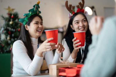 Meslektaşlar, bir ofis ortamında bayram süslemeleri ve hediye alışverişlerinin yer aldığı Noel partisinin keyfini çıkarıyorlar..