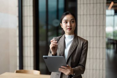 Modern bir ofiste elinde tablet olan profesyonel bir kadın iş ortamında güven ve teknoloji sergiliyor..