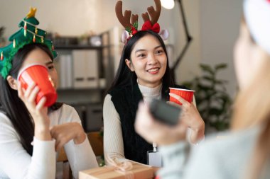 Meslektaşlar, bir ofis ortamında Noel partisinin keyfini çıkarıyorlar. Tatil süslemeleri ve neşeli etkileşimlerle dolu..