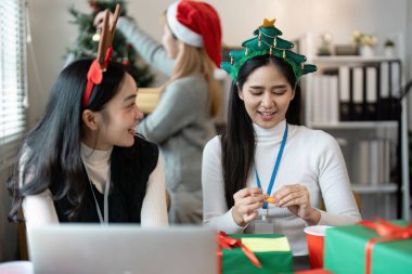 Colleagues in an office setting celebrate Christmas with festive hats, gifts, and tree decorations, creating a joyful holiday atmosphere. clipart