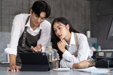 Two young professionals brainstorming in a contemporary office setting, using a tablet to develop innovative startup ideas. clipart