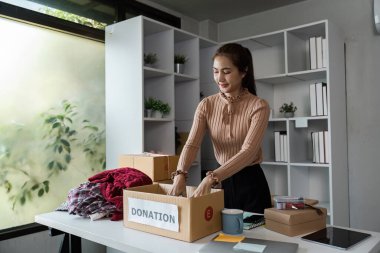 Bir kadın eşyaları bağış kutusuna yerleştirir, modern bir ofis ortamında yardım için giysi ve malzeme hazırlar..