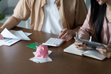Bir çift, bütçelerini planlamak ve verimli bir şekilde para biriktirmek için kumbaranın yanında bir hesap makinesi ve tablet kullanıyor..