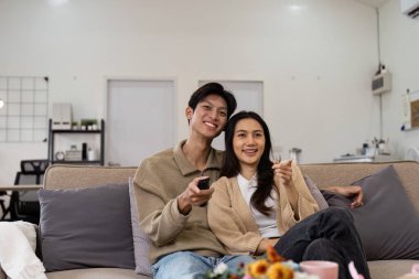 Gülümseyen bir çift, rahat bir akşamın tadını çıkarıyor, rahat, modern bir oturma odasında televizyon seyrediyor..