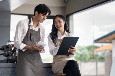 Modern ofis ortamında çalışan iki genç profesyonel, dijital cihazlar ve belgelerle çalışma, takım çalışması ve işbirliği konularını tartışıyor..