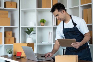 Bir dizüstü bilgisayarda çalışan küçük bir işletme sahibi, çevresi nakliye kutularıyla çevrili, modern online başlangıç ortamını temsil ediyor..