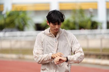 Rüzgarlık giymiş genç bir adam koşu sırasında spor takip cihazını kontrol eder. Sağlık ve sağlığını destekler..