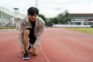 Genç bir adam ayakkabı bağcıklarını koşu pistine bağlıyor. Vücut geliştiren spor, sağIık ve aktif bir yaşam tarzı..