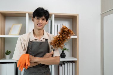 Önlüklü, temizlikçi, modern bir evde ev işleriyle uğraşmaya hazır genç bir adam..