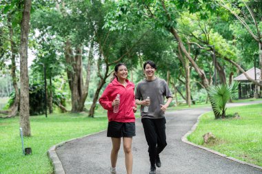 Neşeli bir çift canlı bir parkta koşuyor, sağlıklı ve sağlıklı bir yaşam sürüyorlar, doğanın ortasında..