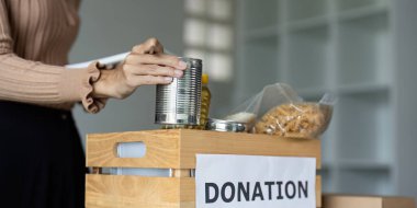 A person organizing canned goods and food items in a donation box, symbolizing charity, community support, and giving back. clipart