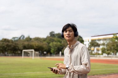 Pistte koşan, kulaklık takan, dışarıda sağlık ve sağlık hizmetlerini destekleyen genç bir adam..