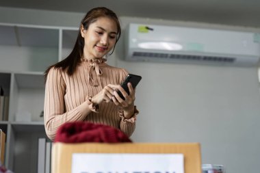 A young woman uses a tablet while organizing clothing donations in a modern office setting, emphasizing sustainability and charity. clipart