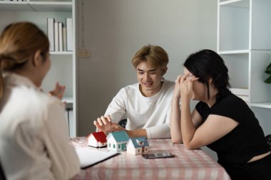 Real estate agent and clients discussing property sale with model houses on table, showcasing home buying process. clipart