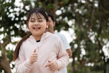 Pembe ceketli neşeli genç bir kız dışarıda koşuyor. Etrafı yemyeşil, güneşli bir günün tadını çıkarıyor..