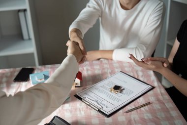 Real estate agent finalizing a property deal with clients, showcasing a contract and house model on a table. clipart