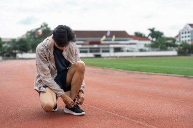 A young adult tying shoelaces on a track, ready for a fitness session. Perfect for themes of health, exercise, and motivation. clipart