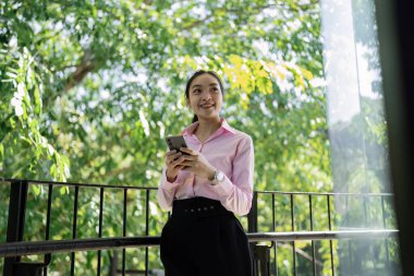 Genç bir profesyonel, akıllı telefonuyla modern iş hayatıyla, ilham verici bir açık hava ortamında harmanlıyor..