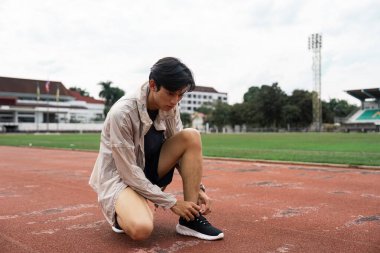 An athlete ties shoes on a track field showcasing dedication and readiness for the upcoming competition. clipart