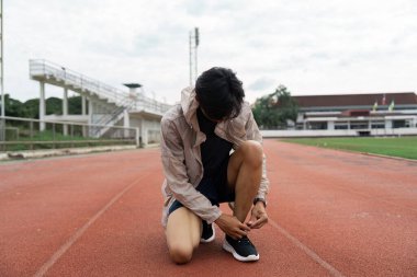 An athlete kneels to tie shoelaces on a track embodying dedication and readiness for competition. clipart